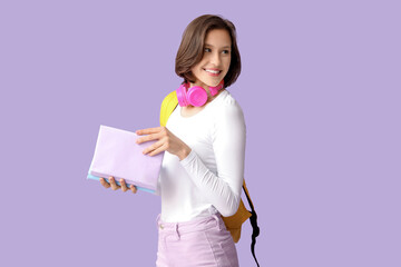 Beautiful female student with headphones, backpack and books on lilac background