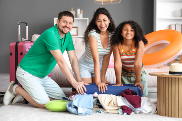 Happy family sitting on floor and packing suitcase for travel at home