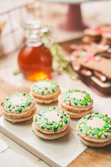 festive macarons, each intricately decorated with hand-painted green wreath designs and tiny red accents, evoking the charm of the holiday season. The delicate cookies rest on a wooden serving board