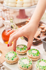 festive macarons, each intricately decorated with hand-painted green wreath designs and tiny red accents, evoking the charm of the holiday season. The delicate cookies rest on a wooden serving board, 