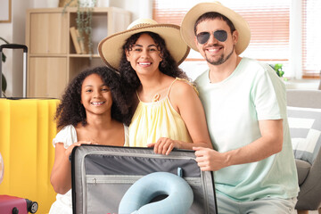 Happy family sitting on floor and packing suitcase for travel at home