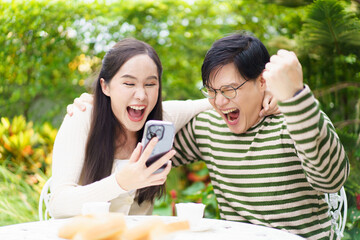 Excited Asian man and woman expressing their happy and satisfied emotion after got a message on smartphone.