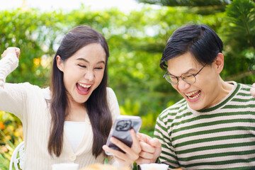 Excited Asian man and woman expressing their happy and satisfied emotion after got a message on smartphone.