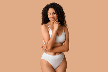 Beautiful young happy African-American body positive woman in underwear on beige background