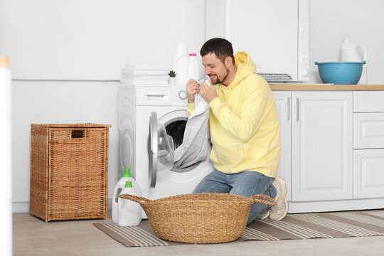 Young man smelling clean laundry from washing machine at home