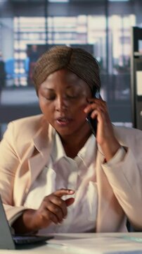 Vertical Video African american general manager answers smartphone call to discuss performance metrics, focusing on business development project. Director multitasking daily operations and analytics