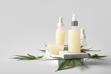 Decorative podiums with bottles of hemp cosmetic oil, sea salt and leaves on grey background