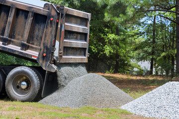 Truck unloads gravel onto grassy area preparing for landscaping work process demonstrates delivery...