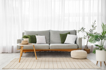 Interior of light living room with sofa, table and pouf