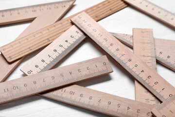 Many rulers on light wooden background, closeup