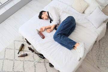 Drunk young businessman lying on bed, top view. Alcoholism concept