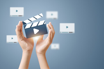 Hands holding a clapperboard with a play icon, representing video production and content creation.