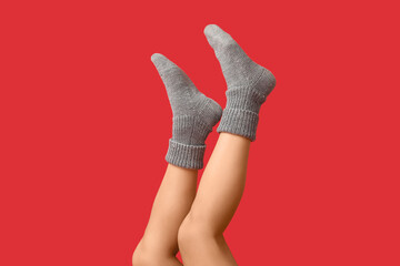Legs of young woman in grey knitted socks on red background