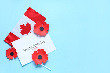Paper poppy flowers with flag of Canada and card on blue background. Remembrance Day