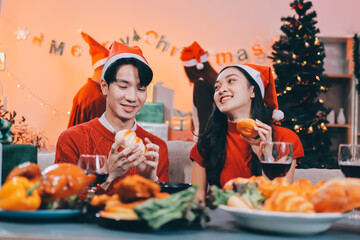 Group of young Asian man and women as friends having fun at a New Year's celebration, holding gift boxes standing by Christmas tree decoration, midnight countdown Party at home with holiday season.