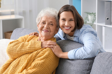 Young nurse hugging senior woman on sofa at home