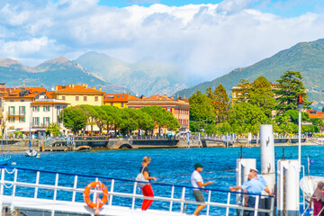 Selective focus on the colorful lakefront village of Menaggio, Italy in summer as passengers walk along a ramp to board a lake taxi boat on Lake Como.