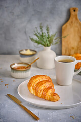 A fresh croissant with a crisp on a white plate with a cup of black coffee on a gray background.