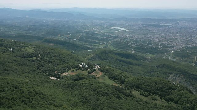 Lush dajti mountain near tirana with a distant cityscape and winding roads visible, aerial view