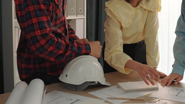 Smart architect and safety engineer discussion about building blueprint on table with architectural document, measurement tools and wooden block scatter around at modern office. Closeup. Delineation.