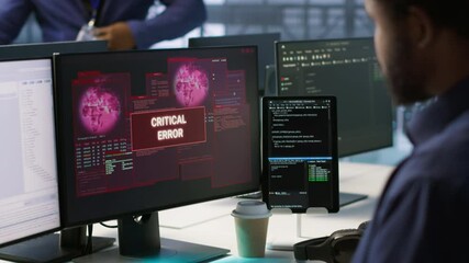 Programmer seeing red critical error popup on computer display in data center, panicking. African american man in server hub spamming keyboard buttons after receiving error, camera A