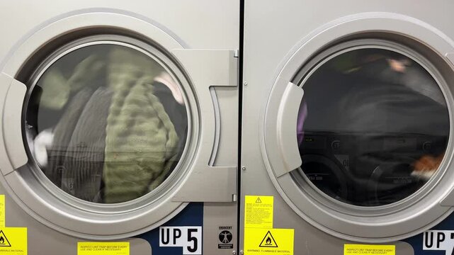 Close-up of laundry spins in industrial machines while patrons wait for their clothes to finish washing in a city laundromat.