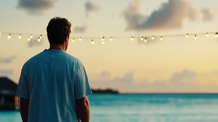 Fototapeta premium Man Staring at Beautiful Sunset Over Water While Standing on a Beach with Decorative Lights Illuminating the Scene, Evoking Peace and Reflection