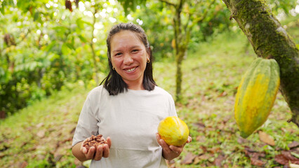 Portrait of smiling southeast asian woman farmer in cacao farm holding harvested pod in one hand...
