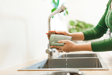 Cleaning, woman in green dress with green ceramic cup in kitchen for hygiene, routine and coffee mug. Female person, washing with water for disinfecting, protection and sink at home 