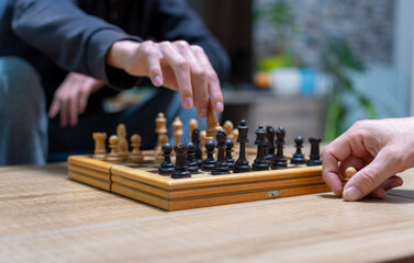 Persons are playing chess on a table at home.