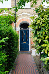 Elegant blue door of traditional london victorian house with checkered pathway and green bushes