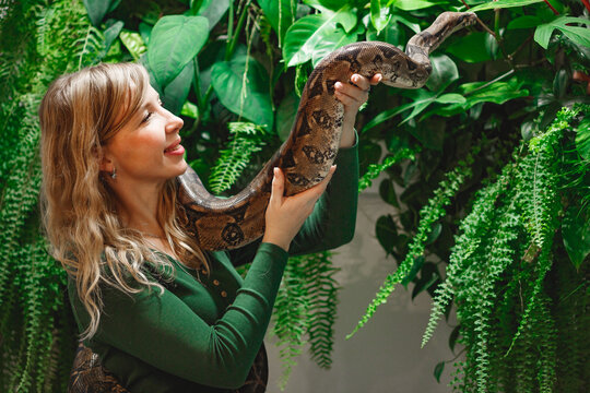 Pretty young woman holding a snake at a reptile encounter, symbolizing an exciting and educational animal interaction, against floral wall
