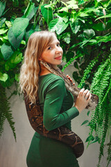 Pretty young woman holding a snake at a reptile encounter, symbolizing an exciting and educational animal interaction, against floral wall
