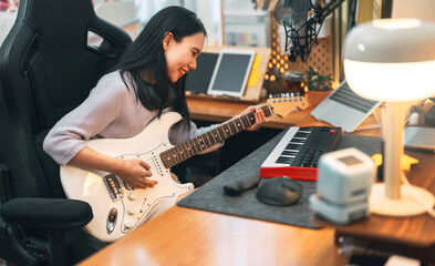 Young asian woman composer playing guitar music with digital technology at home studio