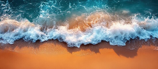 Fototapeta premium Aerial view of ocean waves crashing gently on a sandy beach creating a serene coastal landscape scene