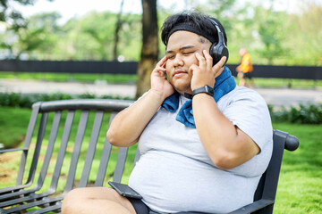 Young Overweight Man Enjoying Music While Sitting on Bench After Doing Workout