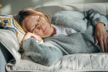 Mature woman is lying on couch at home with closed eyes. Middle aged woman is tired and exhausted....