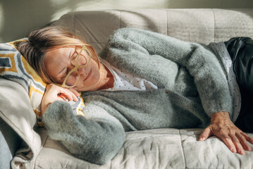 Mature woman is lying on couch at home with closed eyes. Middle aged woman is tired and exhausted....
