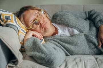 Mature woman is lying on couch at home with closed eyes. Middle aged woman is tired and exhausted....