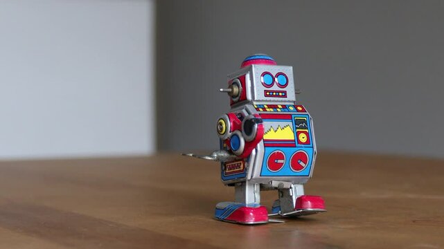 An Asian man winding a tin toy robot and letting it walk on the table, reminiscing about his old days.