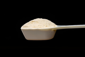 黒背景に計量スプーンで持ち上げたプロテインパウダー