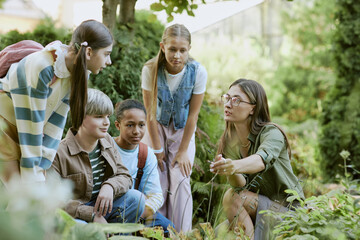 Young female specialist working in local botanical garden showing rare plants to group of teen...