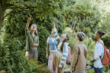 Group of teenagers looking at tree and touching its leaves during tour in botanical garden, copy...