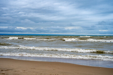 Brown muddy sea waves and dramatic clouds on a beach.
