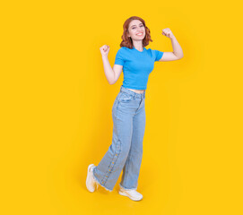 Powerful woman, full body view confident full body 20s powerful woman posing isolated over yellow studio background, copy space. Showing winner pose, clenched fists. Wear casual jean and t shirt.