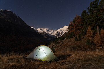 A tent under the night sky in the moonlit Bernina mountain group, Switserland.