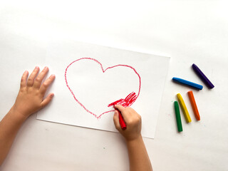 Child drawing heart with crayons on white paper. Creativity and expression