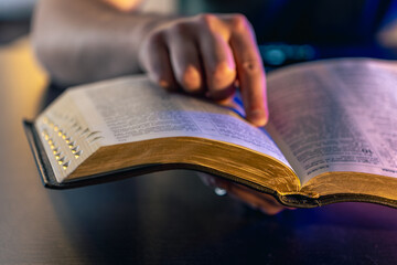 Naklejka premium A man reads the Bible. Male hands on the Holy Bible. Close-up of the Bible.