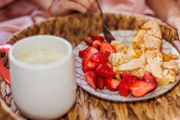 A woman is having breakfast in bed. tray with apple pie and fresh strawberries. morning coffee.