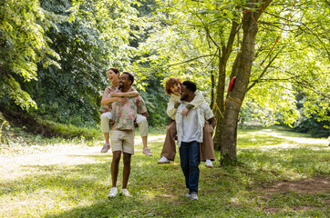 Fototapeta premium Two happy multiracial couples piggybacking in a park